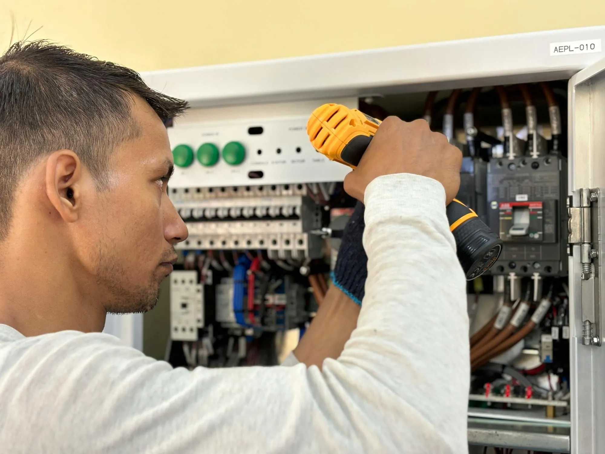 An electrician working on a switchboard with a power drill, fitting new breakers.